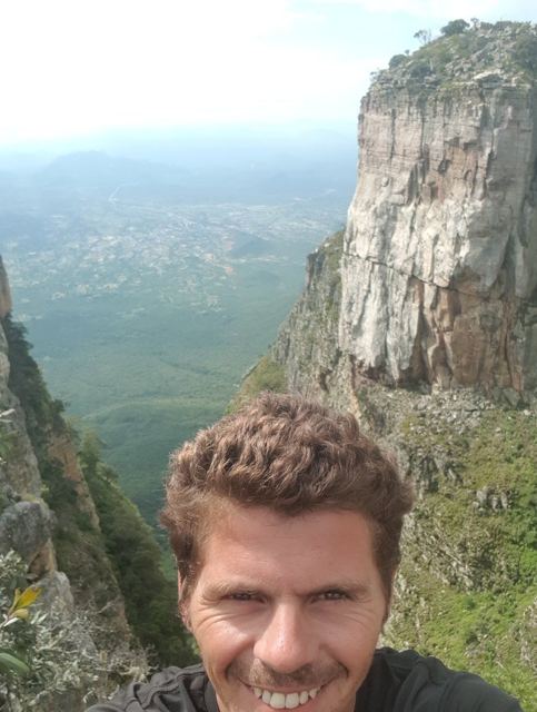 A man taking a selfie at the edge of a huge cliff above a plain in Angola.