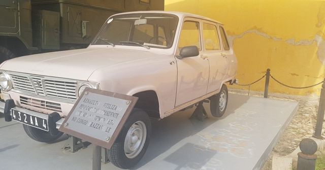A pale pink vintage Renault 4 car on display with an information plaque.
