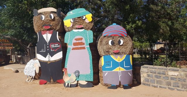 Three colourful painted figures made from hay bales standing outside a building.