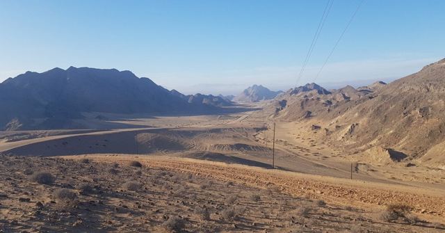 Layers of bare desert mountains under a hazy blue sky.