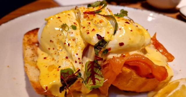 Eggs Benedict with smoked salmon, hollandaise, chilli flakes and microgreens on a white plate.