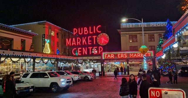 The red neon Public Market Center sign above Pike Place Market at night with festive lights.