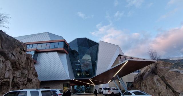 A modern angular building with a faceted glass and metal façade built against a rocky cliff.