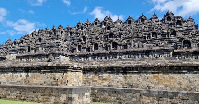 The stone terraces and stupas of Borobudur temple under a blue sky with white clouds.