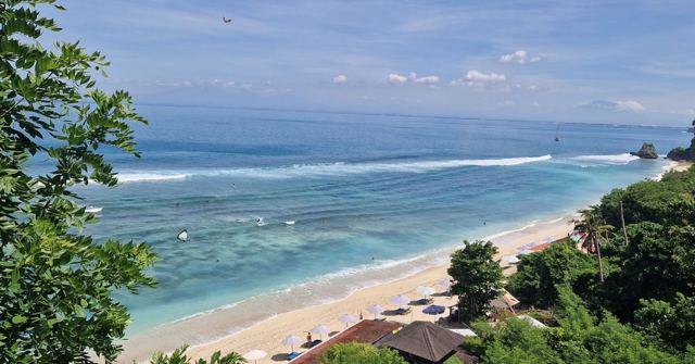 A clifftop view down to a white sand beach with turquoise water and waves breaking on the reef.