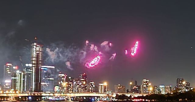 Pink fireworks exploding above Perth's illuminated skyline at night.