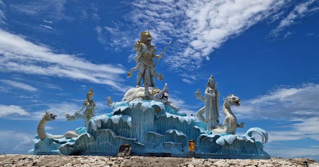 A large blue and white statue of a deity with dragons rising from sculpted waves under a blue sky.