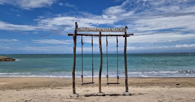 A wooden swing frame on a sandy beach with turquoise sea and blue sky behind.