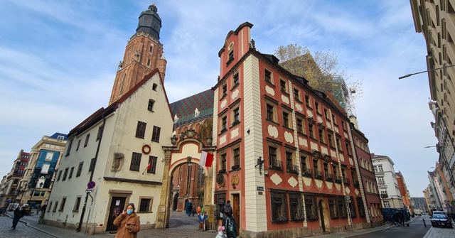Two narrow historic houses joined by an archway, with a tall brick church tower behind.